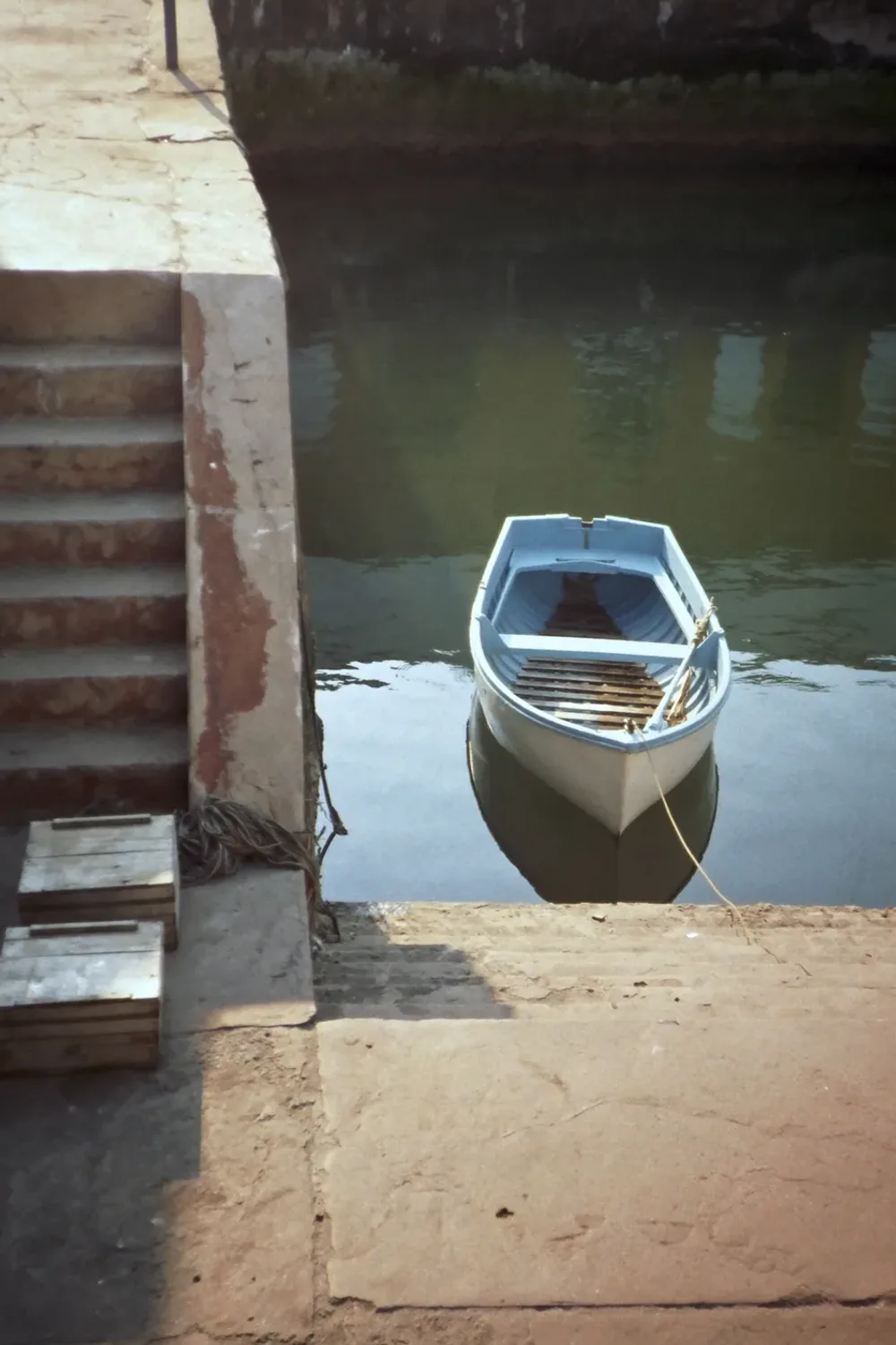 A small pale blue rowing boat moored beside stone steps in a quiet harbour