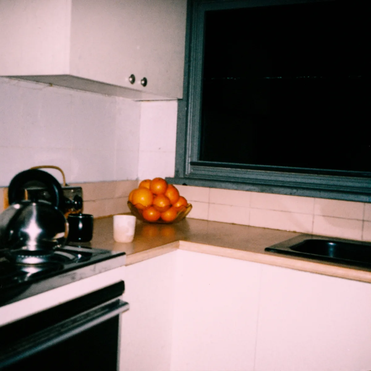 Kettle and oranges on a kitchen counter after dark, flash on